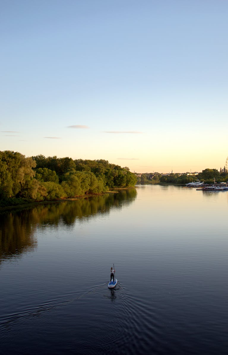 A peaceful aerial view of a river and greenery with a lone paddleboarder captures summer tranquility.