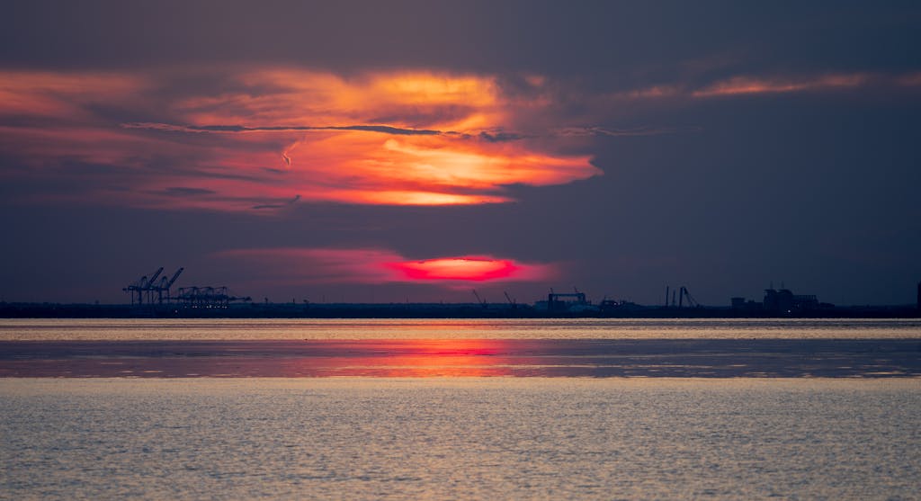 Experience a dramatic sunset over Daphne, Alabama's port with vivid colors and serene reflections.