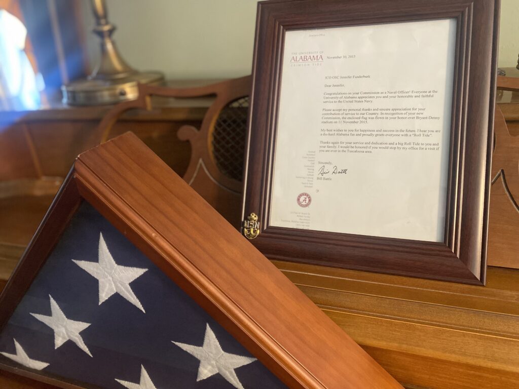 a letter in a picture frame from the University of Alabama and a folded flag
